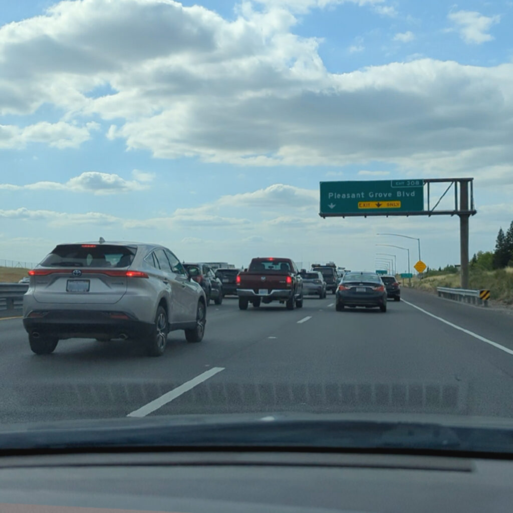 The image shows a view from inside a car on a highway approaching signs for Interstate 80 East and Highway 65 with traffic ahead.